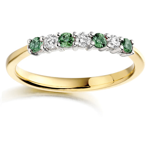 A seven stone ring featuring alternating emeralds and diamonds, set in a yellow gold band.